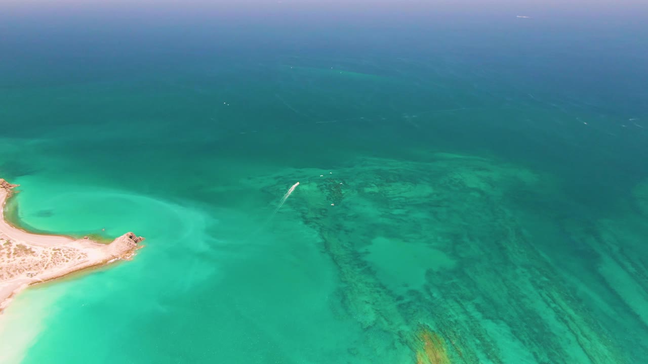 Sandy coastal point beside turquoise water with darker reef patches offshore.