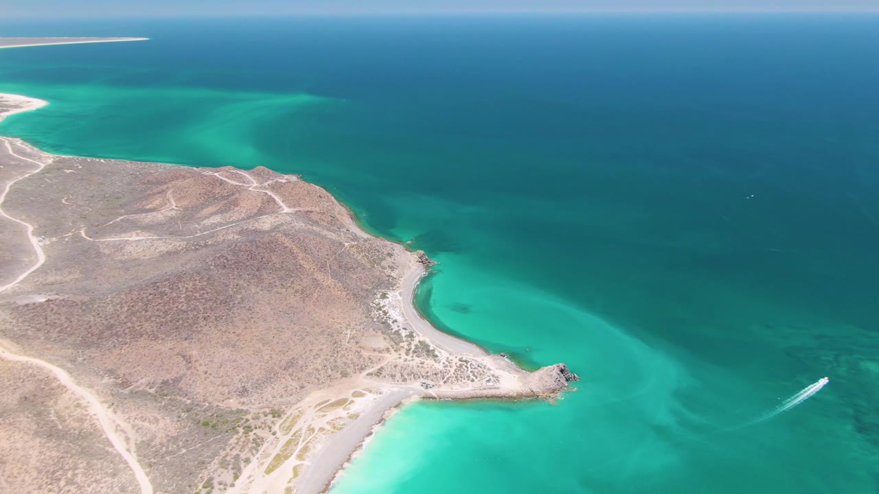 Aerial view of a rocky coastal peninsula beside turquoise water and open sea.