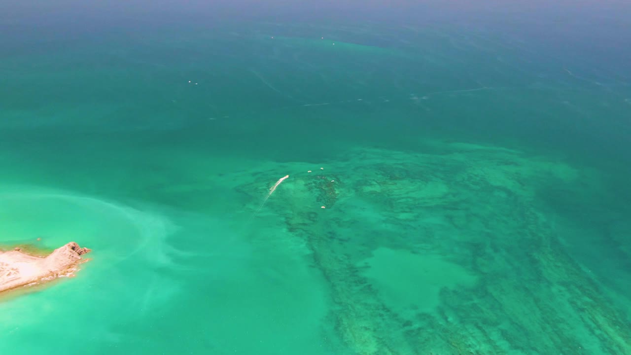 Turquoise ocean water, coral reef, and a small sandy islet at the left edge.