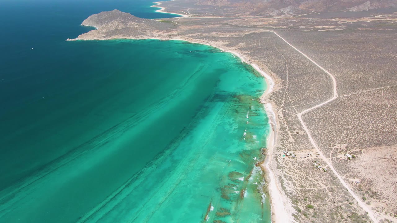 Closer aerial view of turquoise shallows along a sandy shore