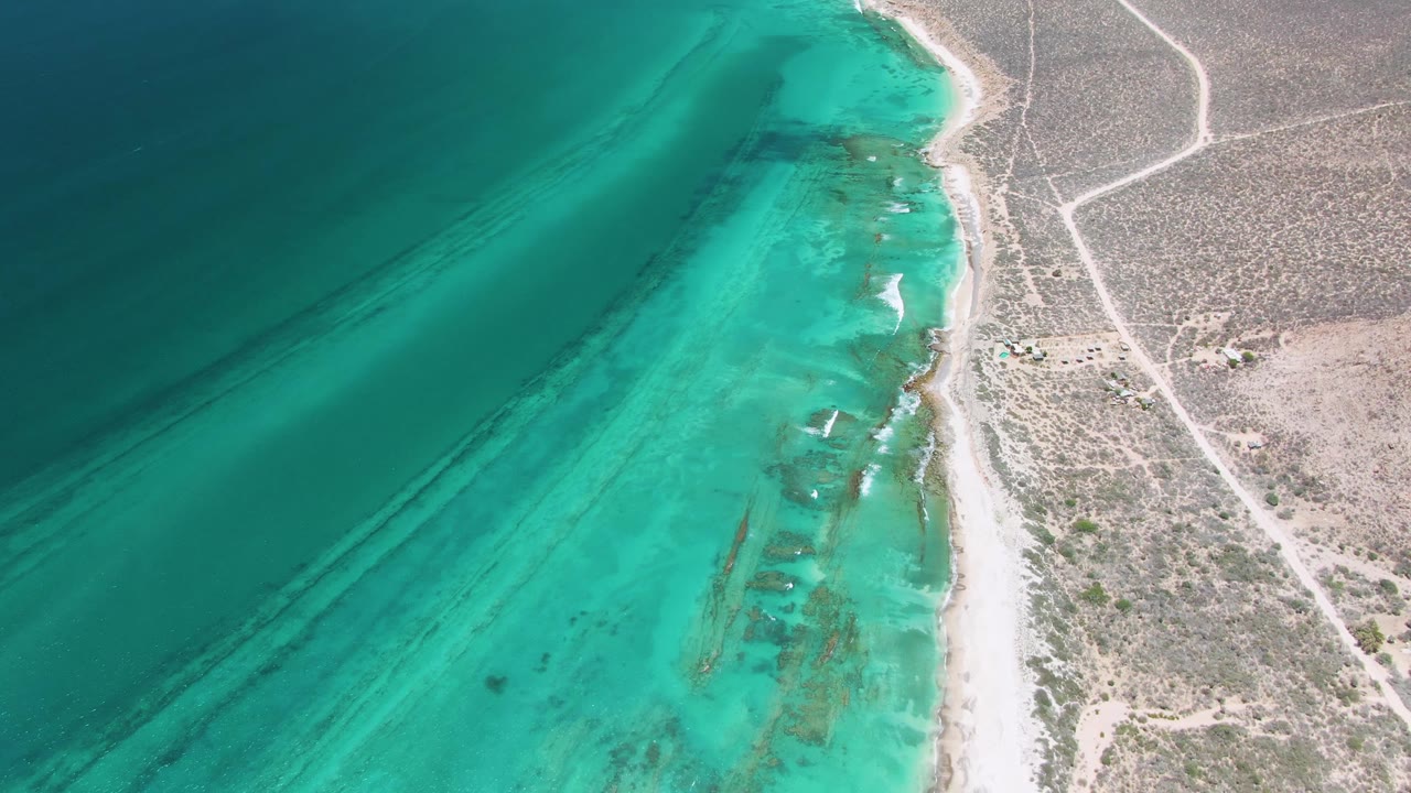Aerial view of turquoise shoreline beside arid land and dirt roads.