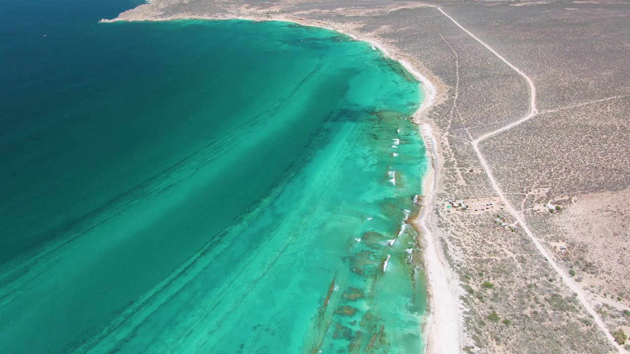 Curving beach between clear turquoise water and dry coastal terrain.