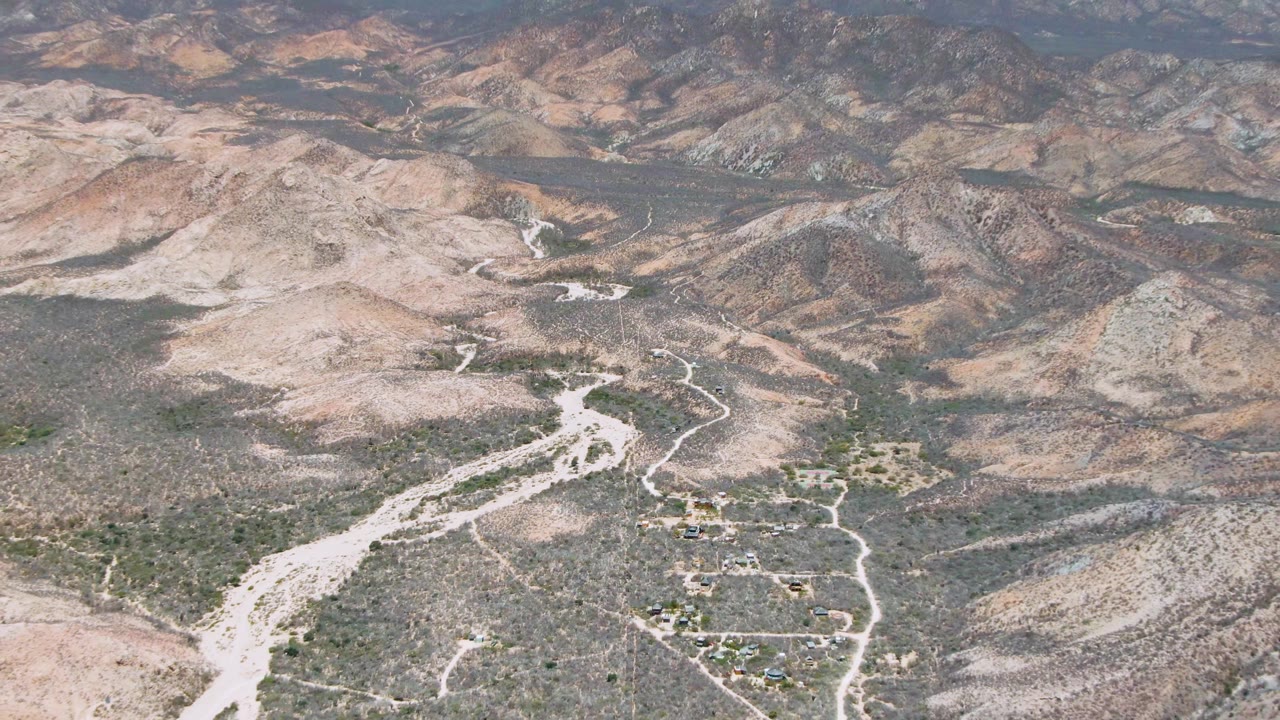 High aerial view of a desert valley with dirt roads and scattered small structures.