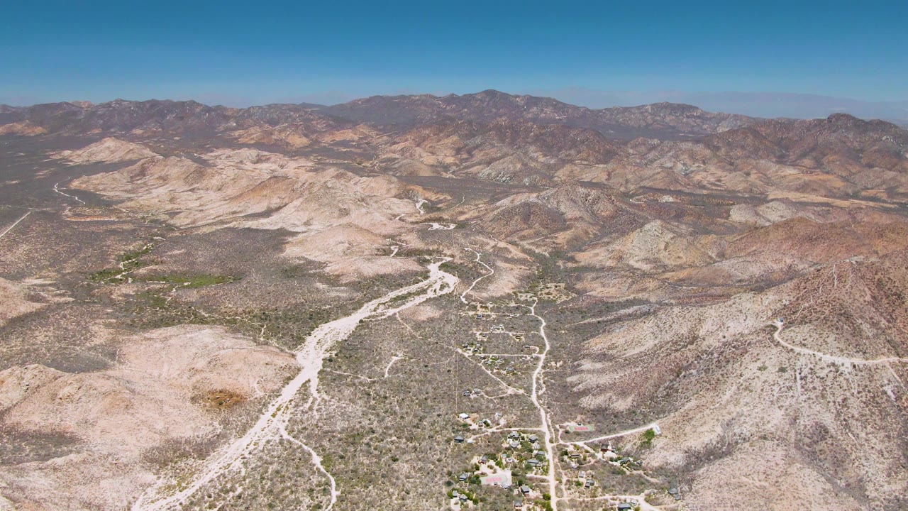 Aerial desert landscape with dirt road, small structures, and mountains.