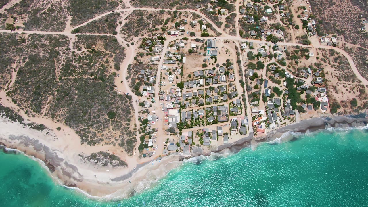 Aerial view of surf meeting a sandy and rocky shoreline below homes