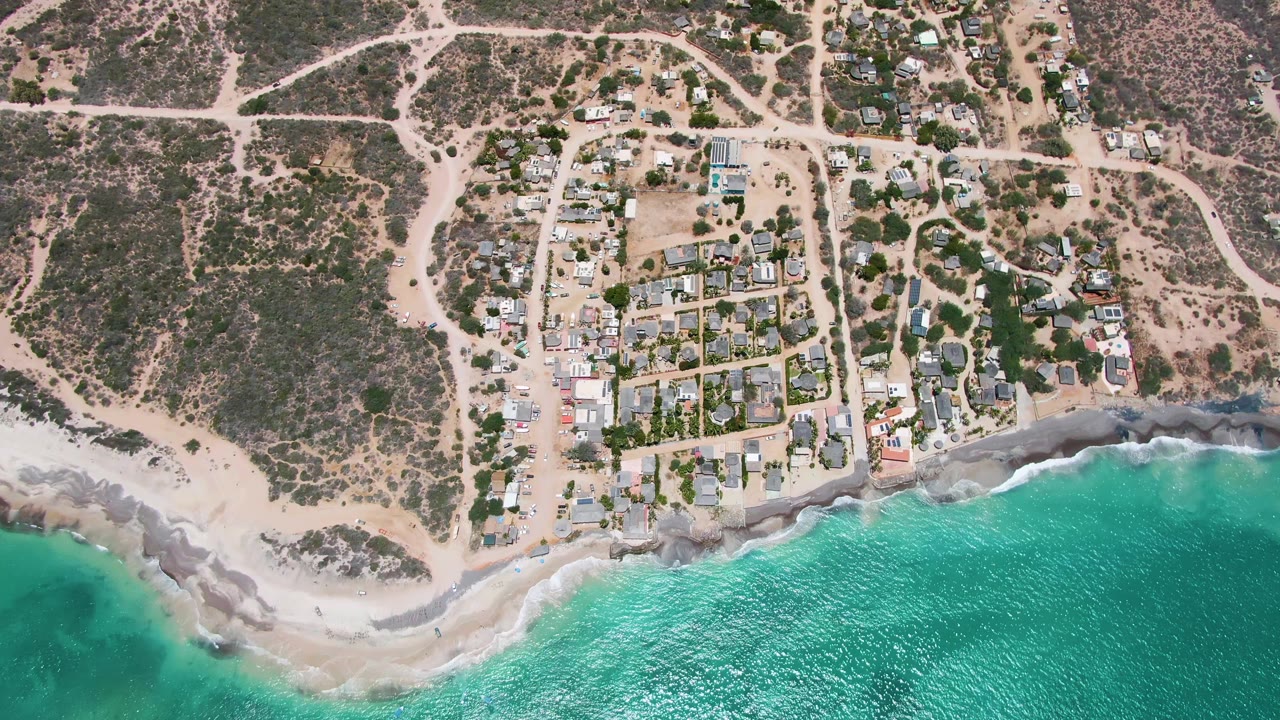 Drone view of residential blocks above a beach with gentle waves.