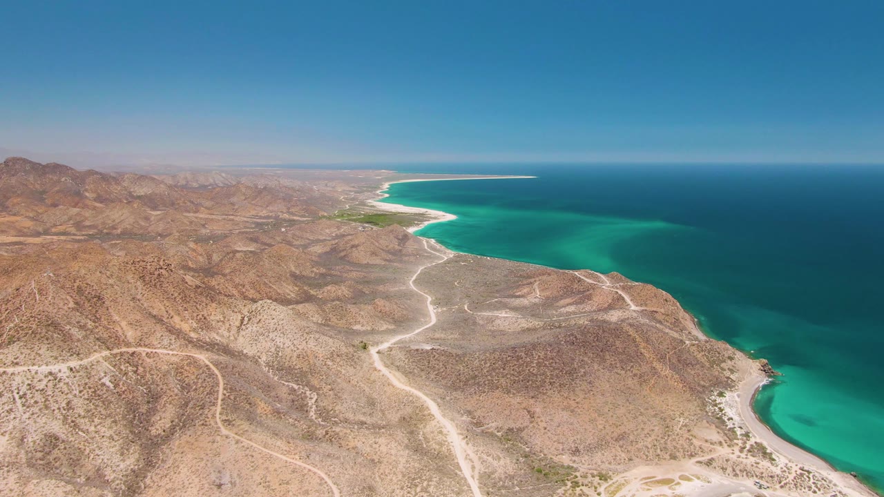 Aerial view of rocky desert hills, winding dirt roads, and turquoise coastline.