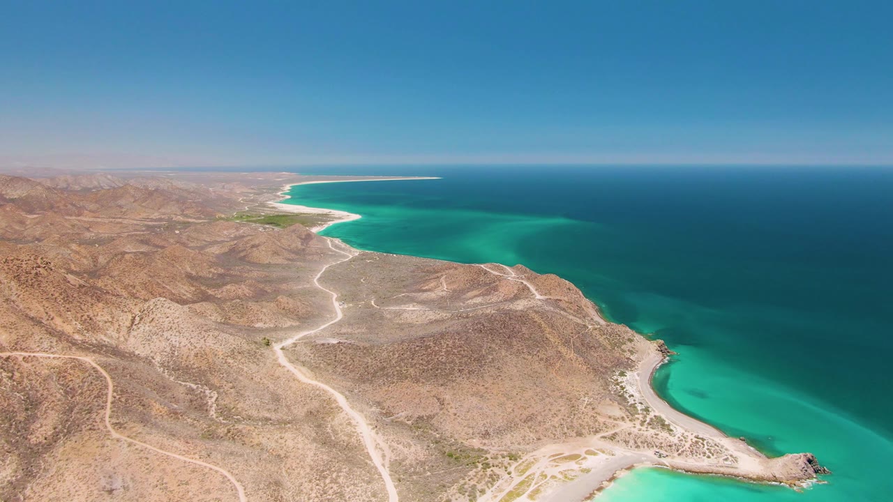 High aerial of sandy desert roads running along a turquoise bay.