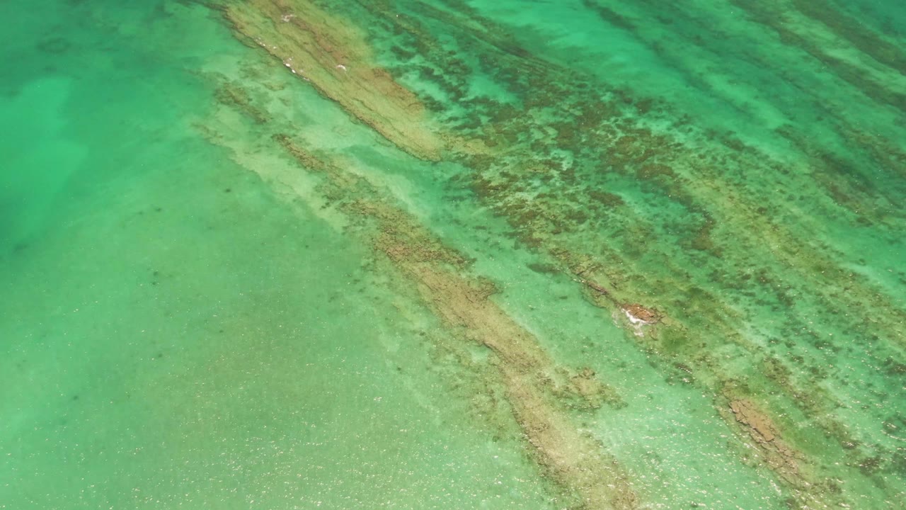 Aerial view of green water and diagonal coral ridges under the surface.