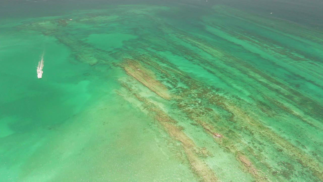 Small white boat over turquoise water and reef bands
