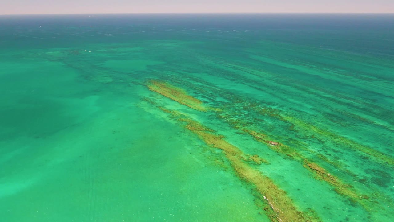 Aerial view of turquoise ocean water with coral reef bands below the surface.