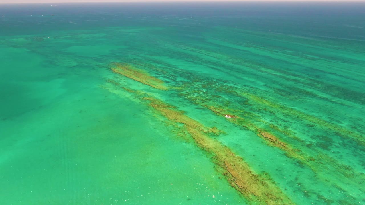 Aerial view of turquoise shallow water over coral reef patterns.