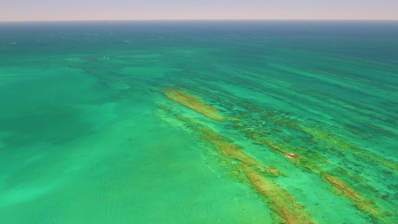 Aerial view in Cabo Pulmo, Baja California Sur with reef color bands extending across clear shallow ocean and no visible people or vessels.