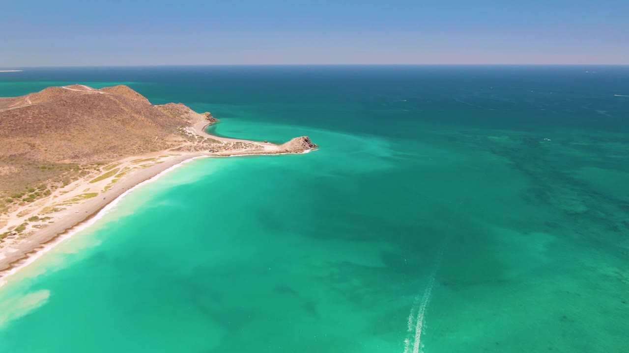 At 0:02, the Cabo Pulmo coast fills the left side while open turquoise and darker blue ocean spread to the right under a clear sky, with no visible people.
