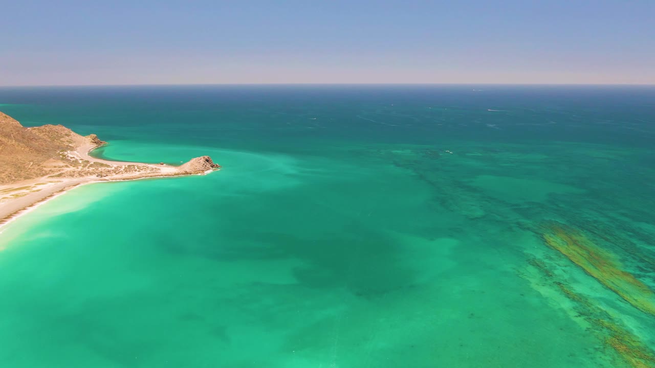 Aerial view of turquoise water beside a sandy shore and rocky headland.