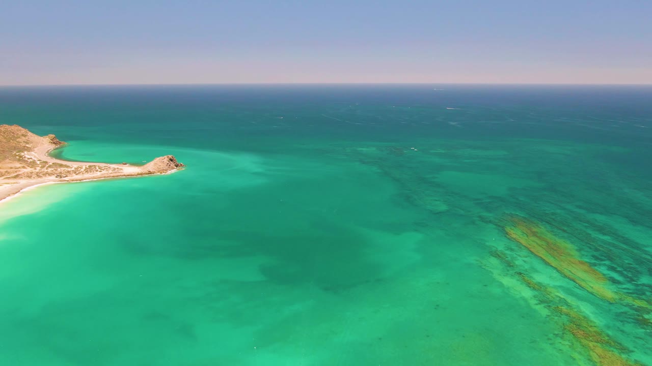 Fourth frame of Cabo Pulmo places the sandy shore and rocky point along the far left edge, with open turquoise water dominating the foreground and no visible people.