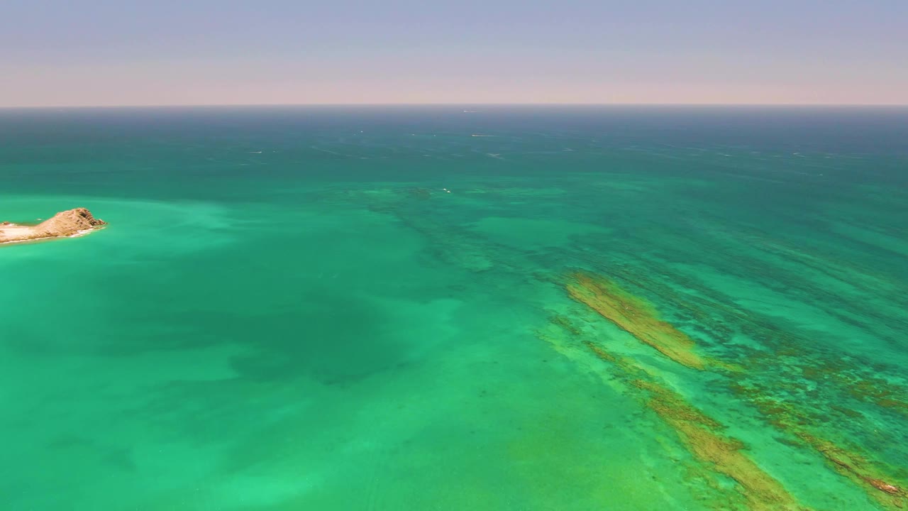Turquoise ocean with a small rocky island and coral reef bands
