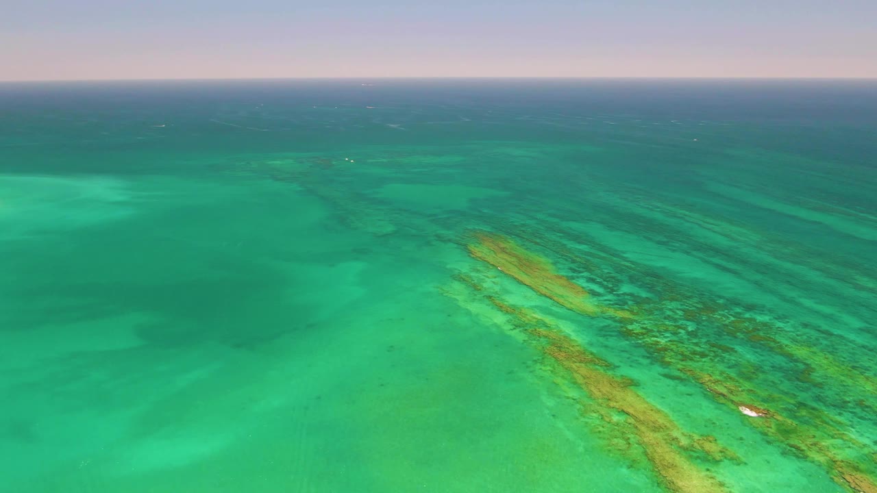 Turquoise ocean with a diagonal reef and small white boat near the lower right