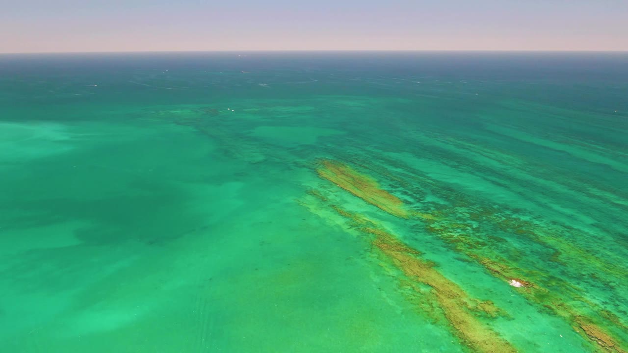 Aerial view of Cabo Pulmo turquoise water with the reef running from lower center toward upper right, a small white boat along the reef edge, and no visible people.