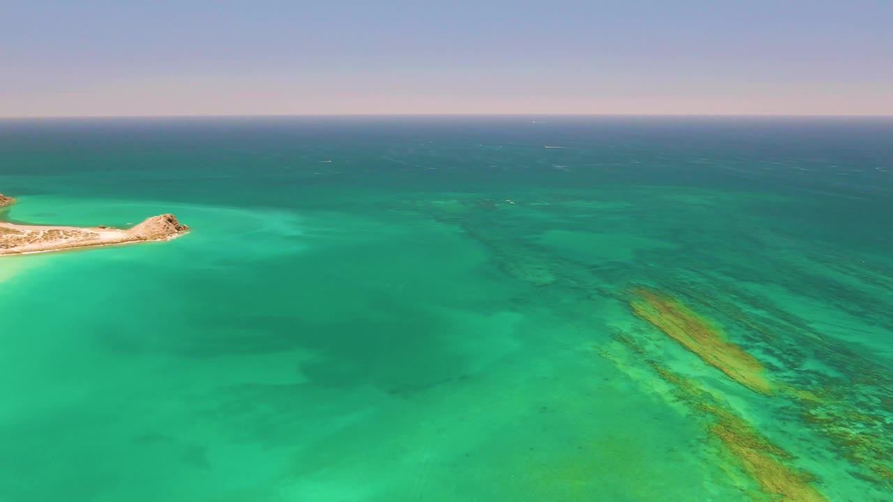 Aerial view of left-edge island and broad turquoise water with seabed patterns.
