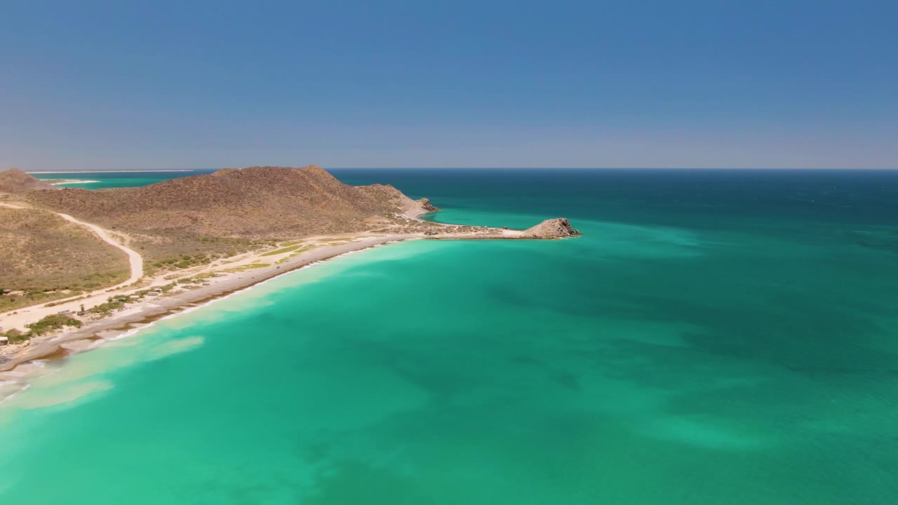 Turquoise bay water with sandy shoreline, road, and low dry hills