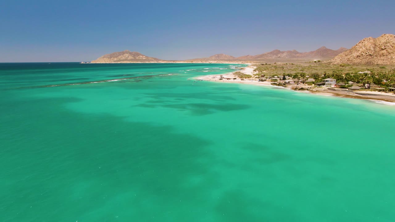 Turquoise coastal water fills the foreground with beach, hills, and buildings in the distance.