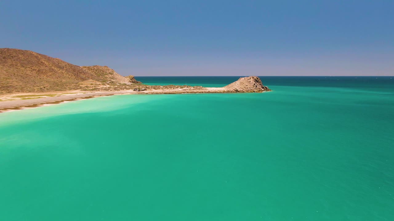 Cabo Pulmo water shows subtle ripples below a high horizon, with the sandy cove and rocky point stretching across the upper frame and no visible people.