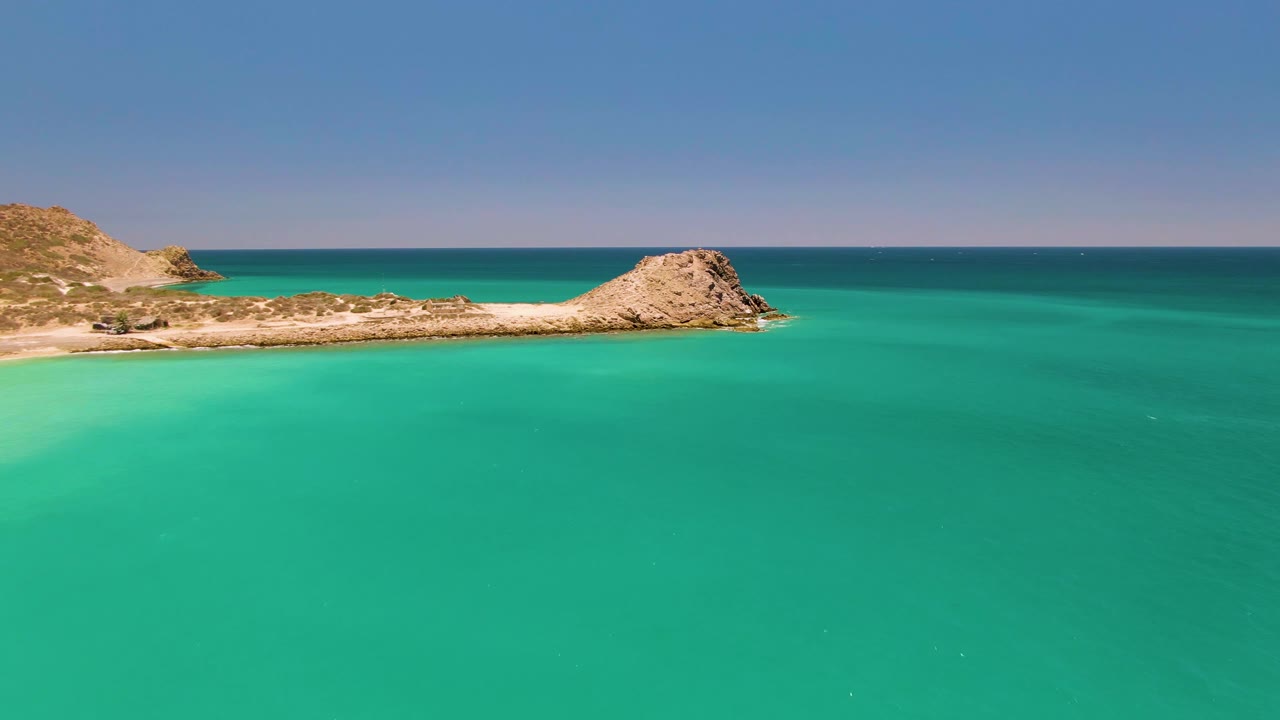 Turquoise sea with rocky point and pale sandy coastline.