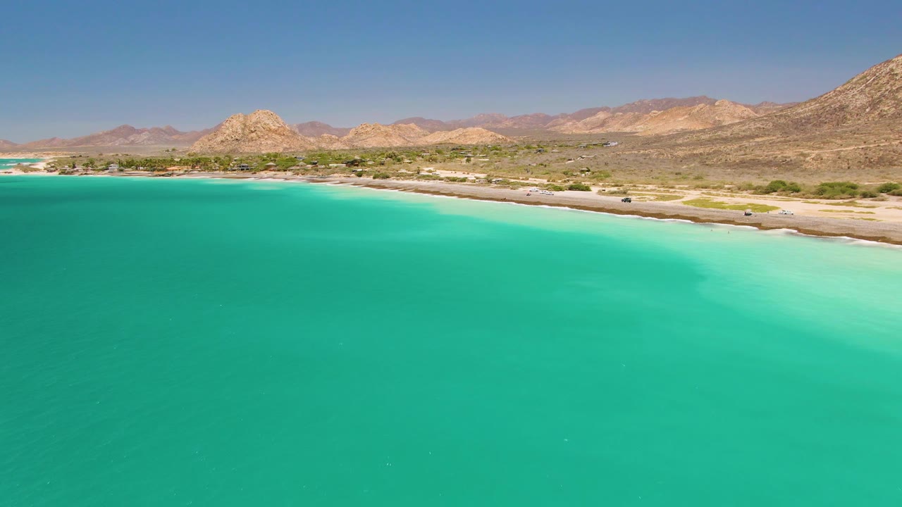 Coastal road with vehicles between turquoise water and rocky hills