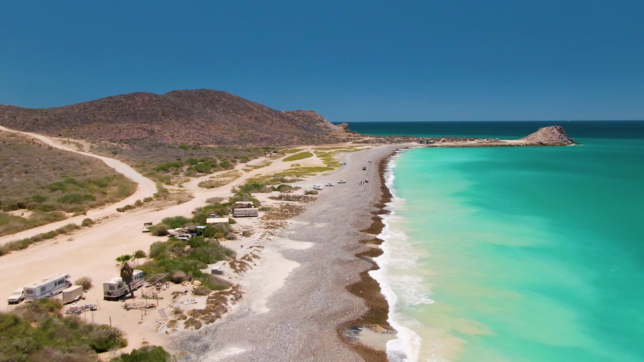 Aerial view of vehicles near beach scrub beside a turquoise shoreline.