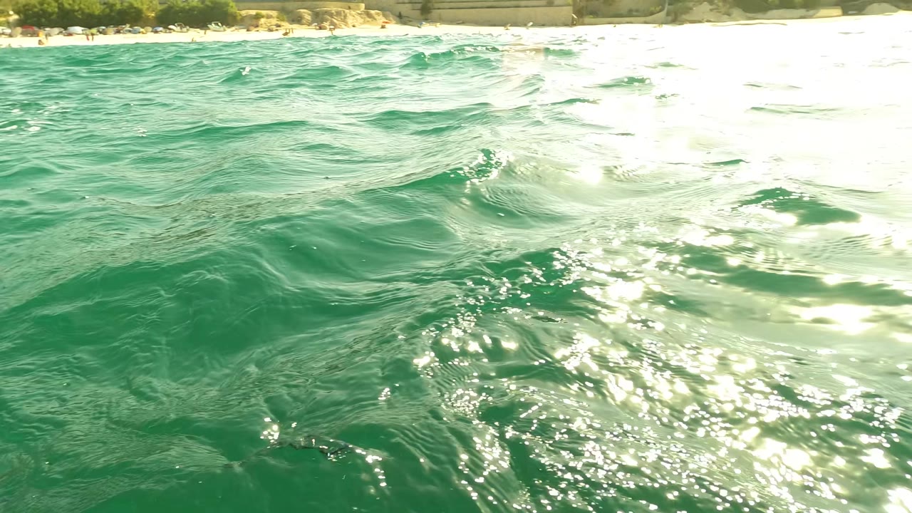 Turquoise ocean surface in Los Barriles, Baja California Sur, with bright sun glare on the right and a distant shoreline at the top edge.