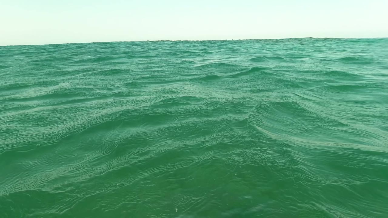 Low ocean surface view with green waves and a distant horizon.