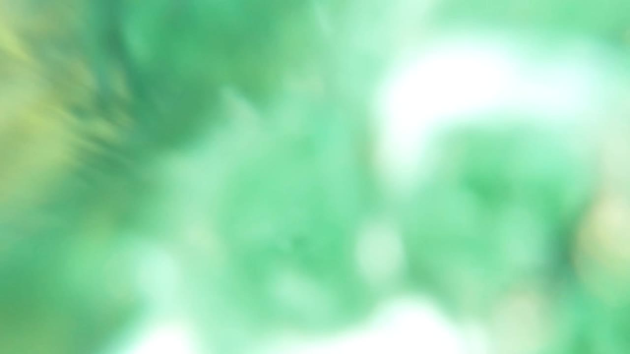 Soft, blurred underwater frame in Los Barriles with green water, indistinct rock shapes, and bright refracted light patches, with no visible people.