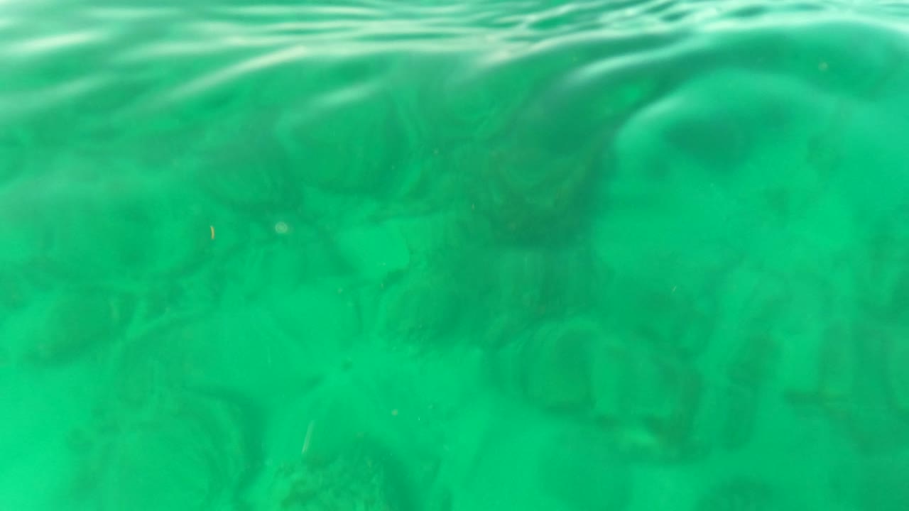 Underwater view in Los Barriles, Baja California Sur, with turquoise water, a soft rocky seabed, rippled surface texture, and no visible people.