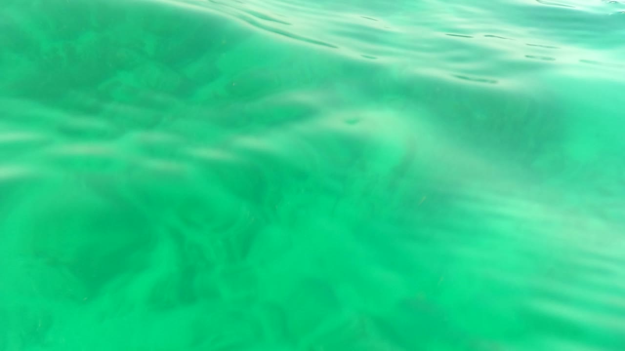 Underwater surface ripples above a hazy green rocky seabed.