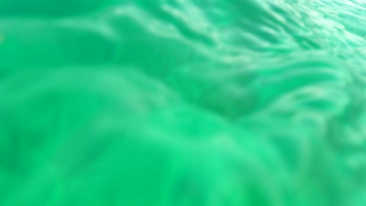 Underwater frame in Los Barriles, Baja California Sur, Mexico, looking up through green water at a softly rippled ocean surface with no visible people.