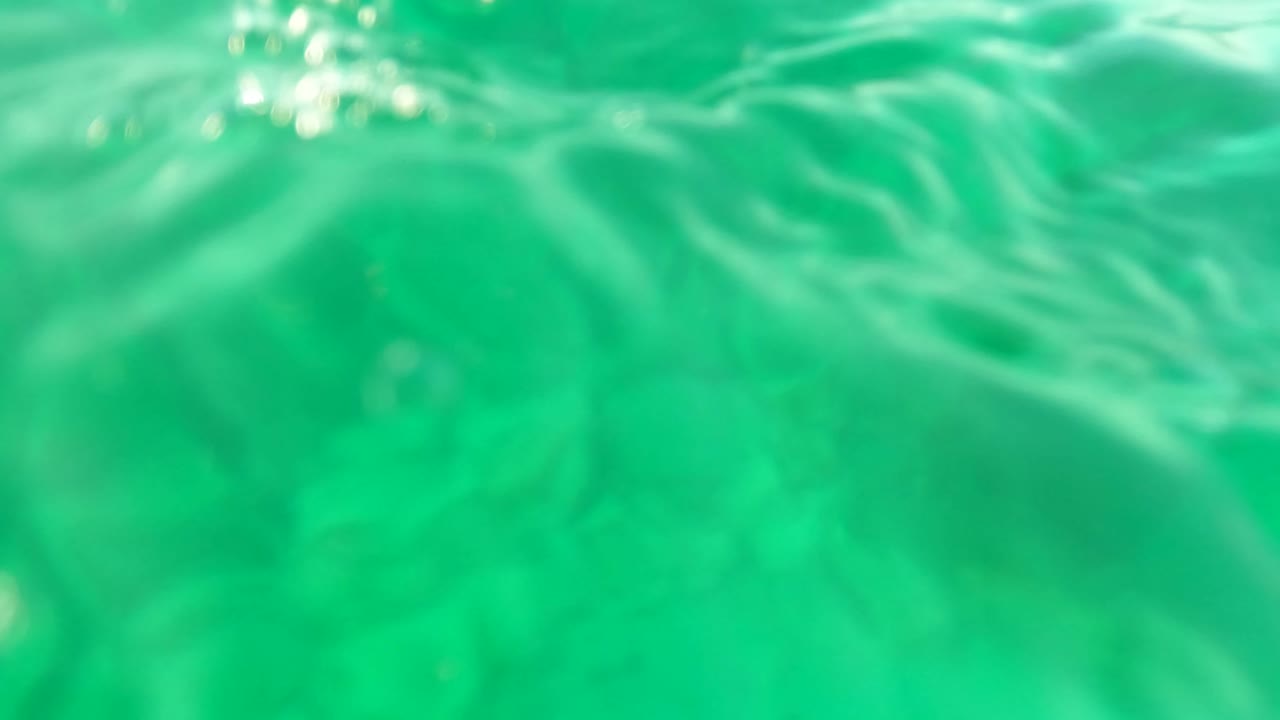 Green underwater view in Los Barriles with the water surface close overhead, brighter ripples near the top, and no visible people.