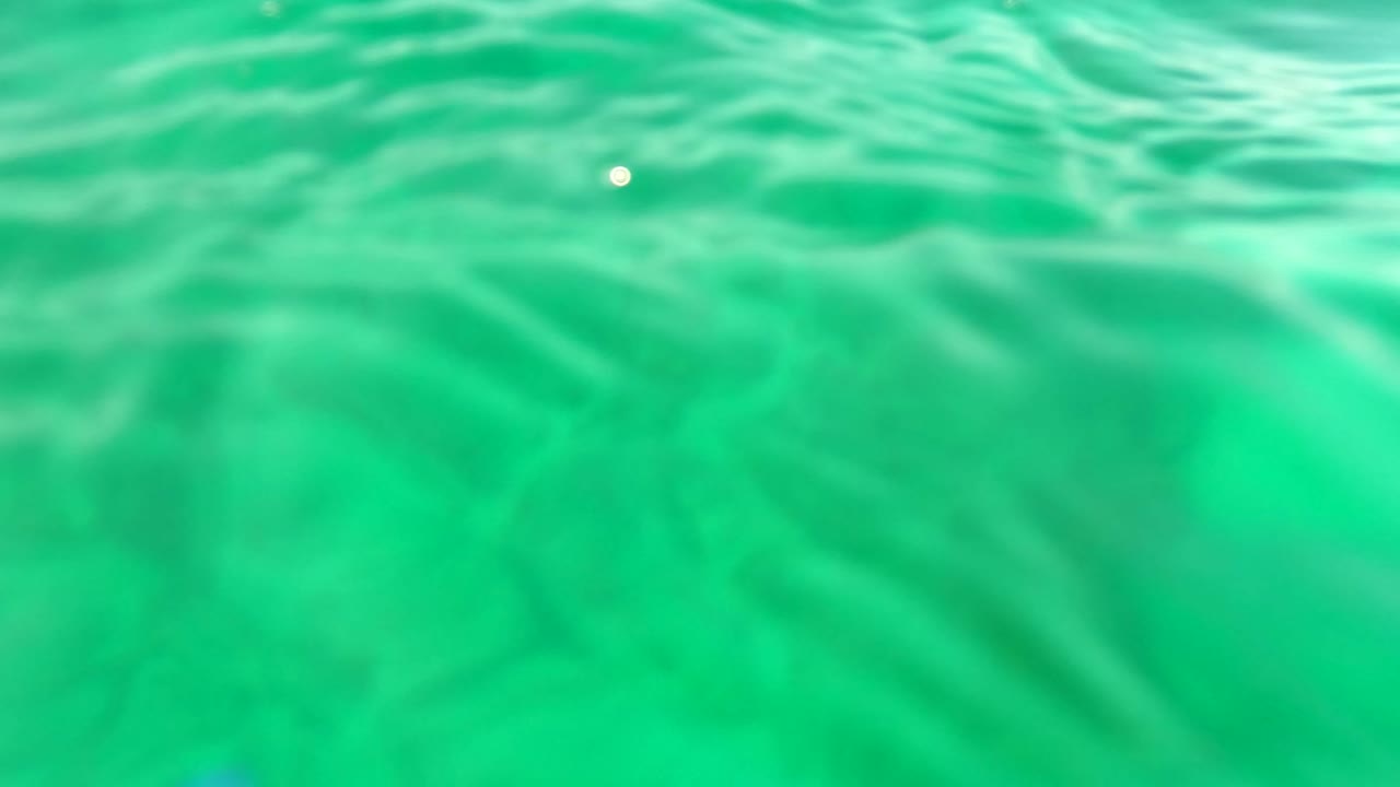 Underwater Los Barriles frame showing textured surface waves across the upper portion and hazy green water beneath, with no visible people.