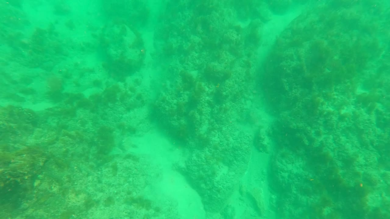 Second frame from Los Barriles, Baja California Sur showing reef rocks and sandy channels under green water, with no clearly visible people.