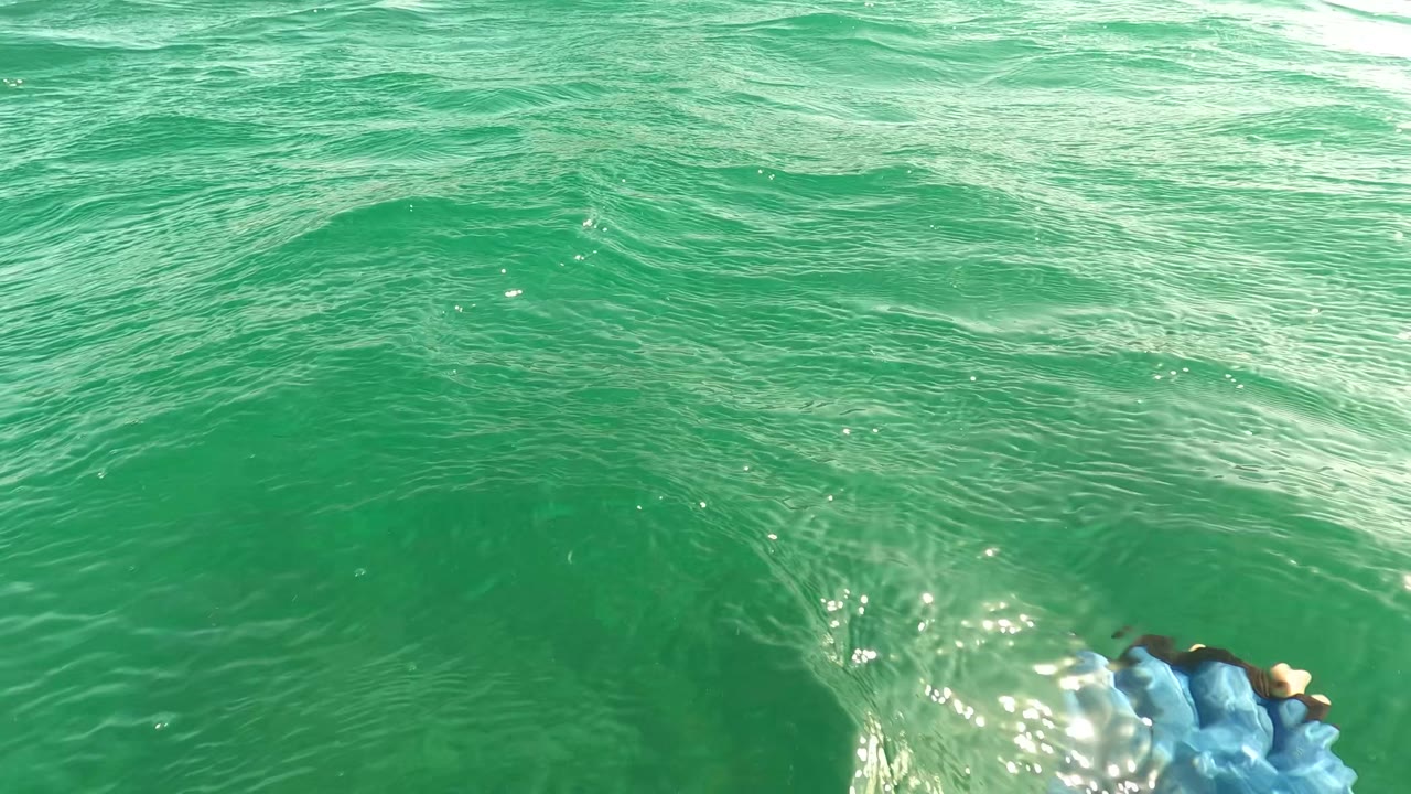Near-surface ocean view in Los Barriles BCS Mexico, with textured green waves and a small blue object partly visible at the lower edge, no visible people.