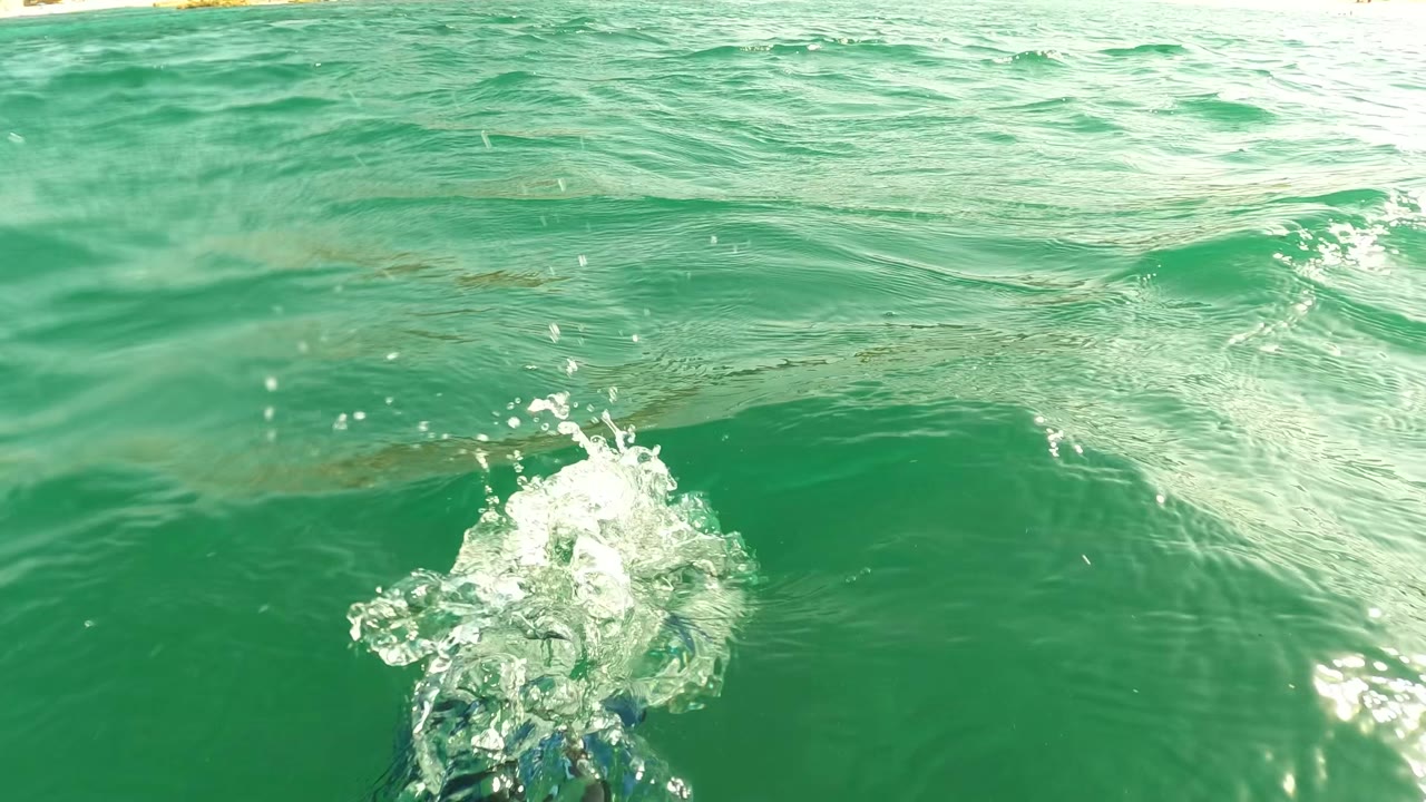 Surface-facing frame from Los Barriles, Baja California Sur, showing a bright splash entering green ocean water with ripples and no visible people.