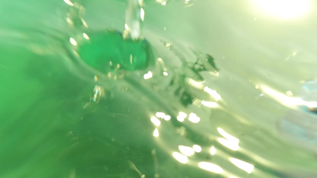 Close underwater view in Los Barriles, Baja California Sur, with green water filling the frame, bright highlights at the upper right, and wavering surface distortion, with no visible people.
