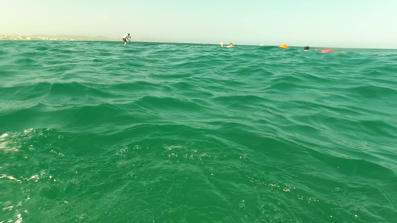 Ocean surface with buoy line, swimmers, and a blue swim fin near the lower right.