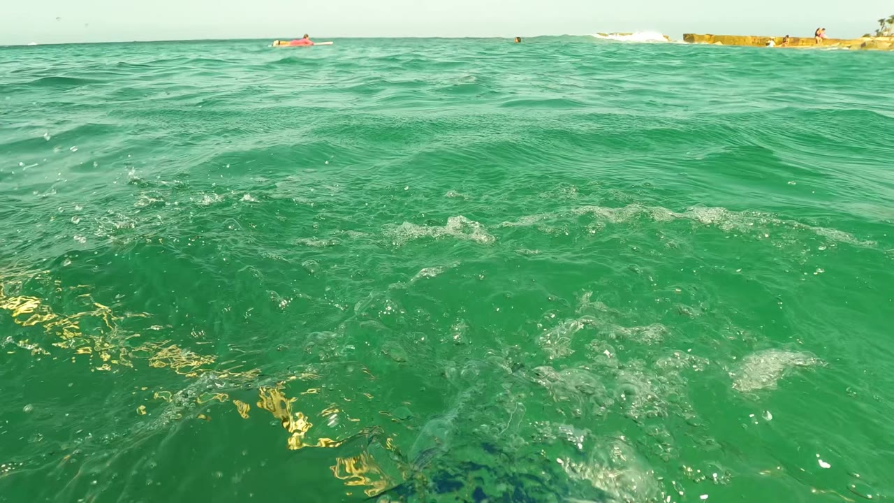 Green ocean surface with low horizon, distant rocks, and a small red craft.