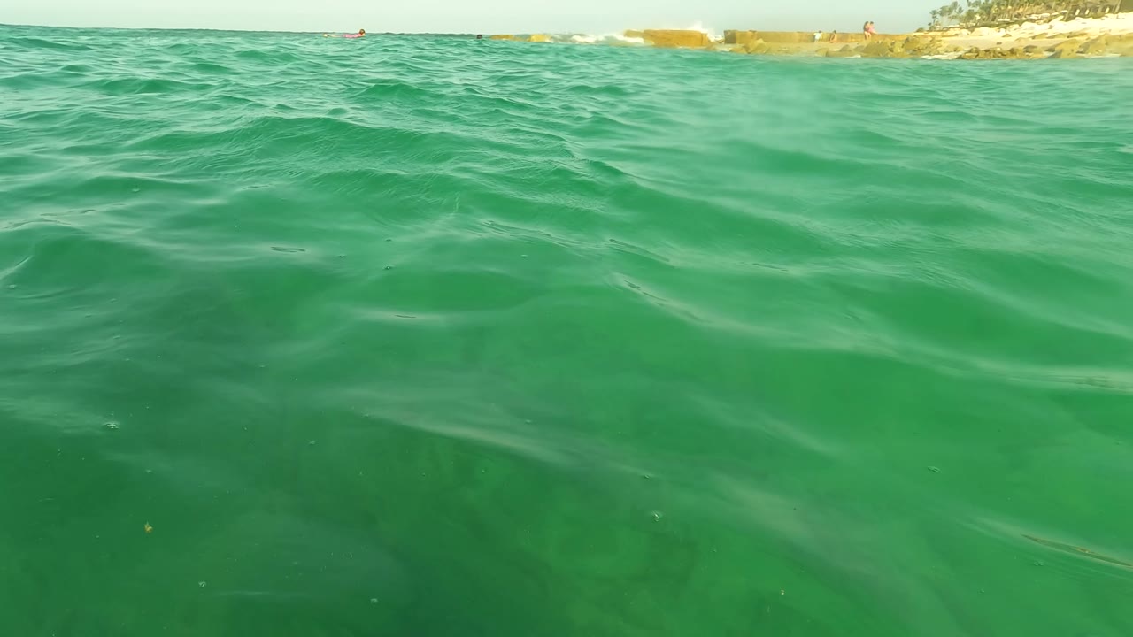 Ocean surface near a beach with small waves and shoreline in the distance.