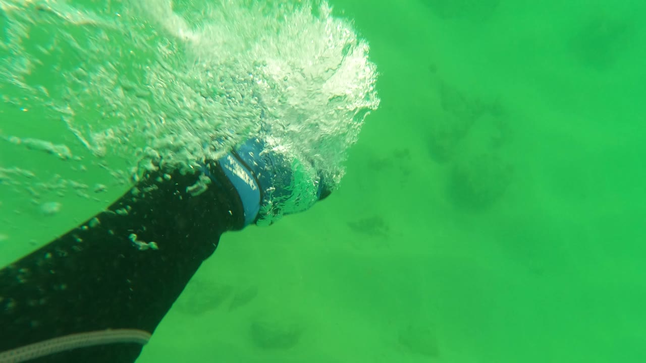 Swimmer's arm and gloved hand push through green water with bubbles near the surface.