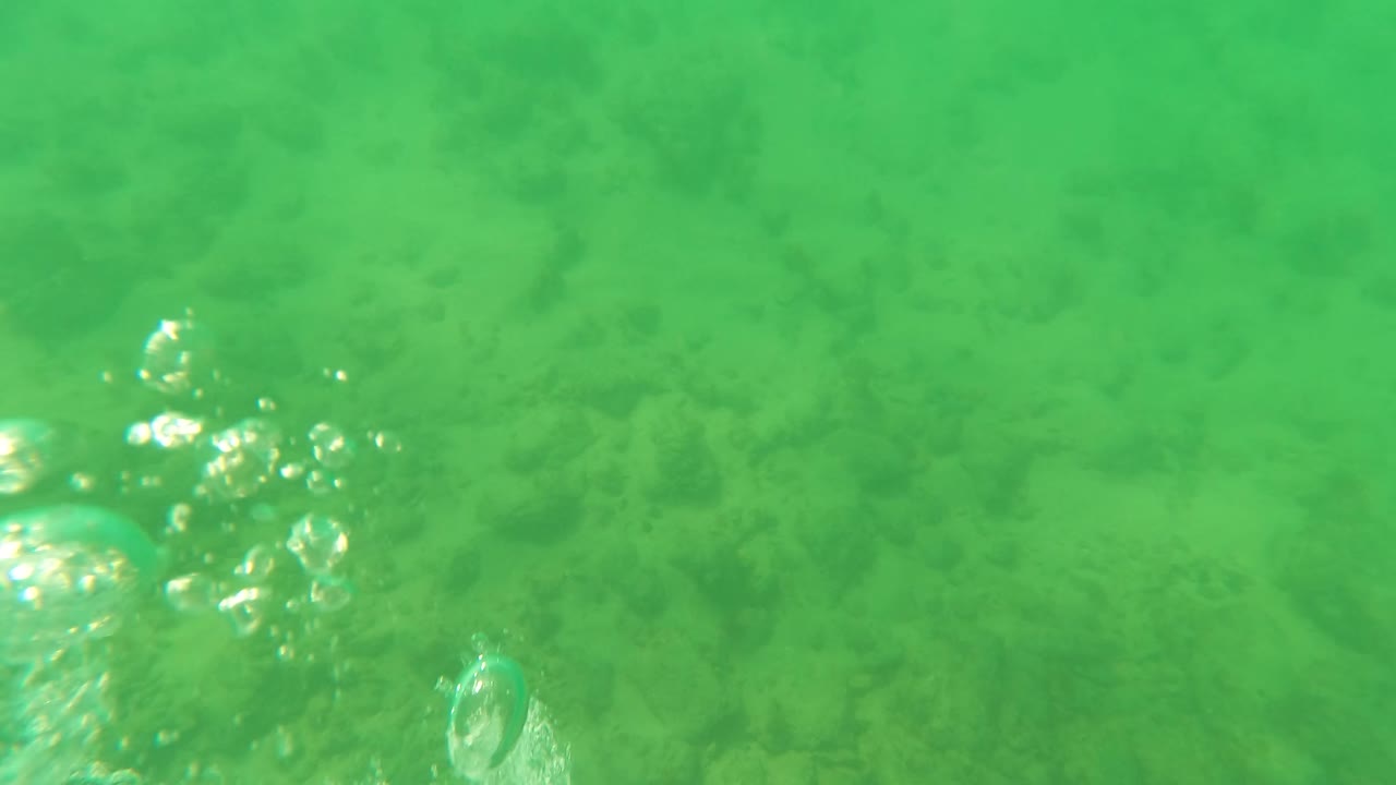 Green underwater frame in Los Barriles with bubbles near the center, mottled seabed below, and no visible people.