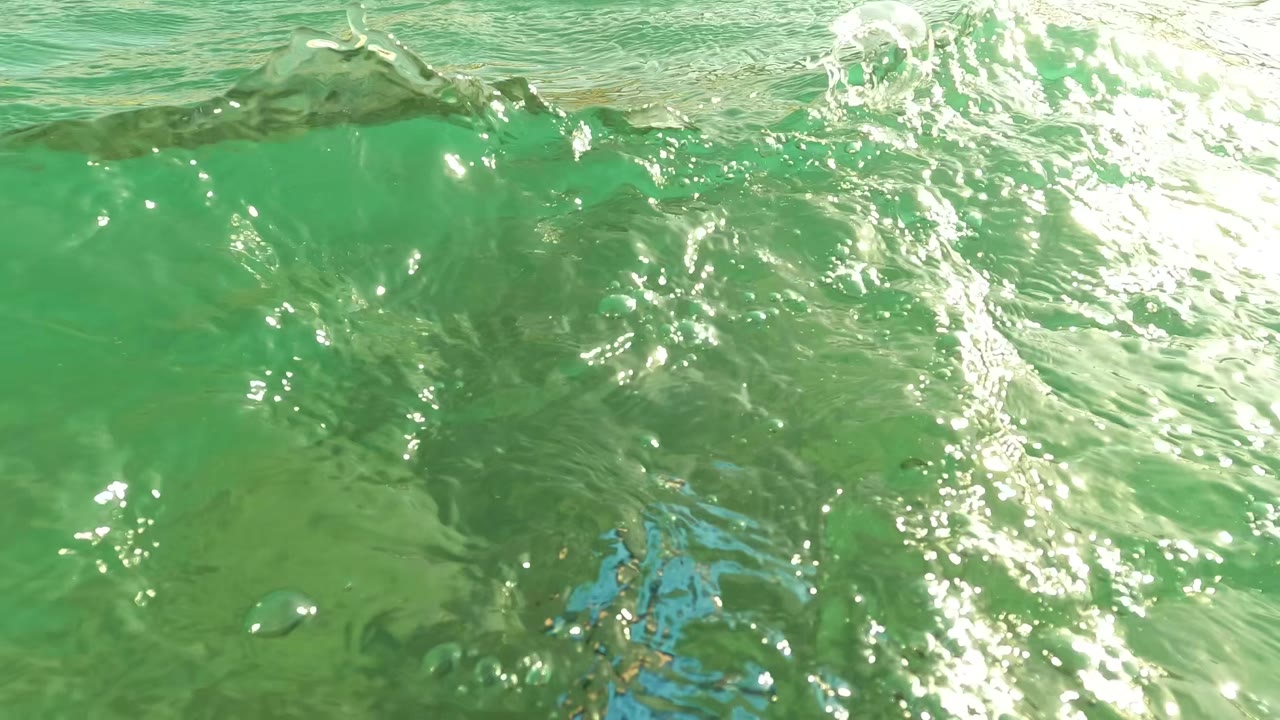 Close surface view in Los Barriles with bright glare on green water and a blue shape partly visible near the bottom, with no visible people.