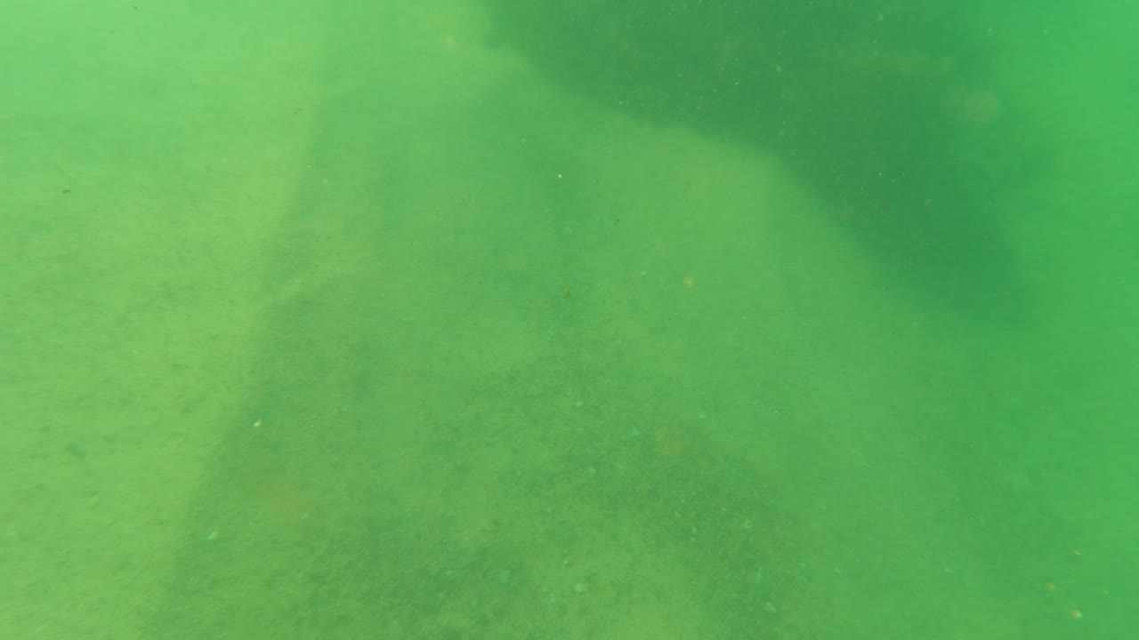 Green underwater view of rusted marine growth on a sandy seabed.