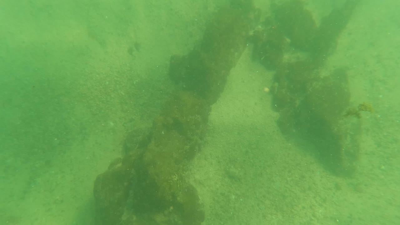 The structure appears more vertical in the green underwater view near Los Barriles, with dark growth hanging over a sandy seabed and no visible people.